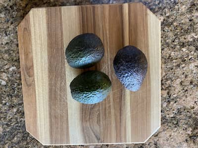 3 avocados on a wooden cutting board.
