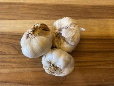 3 heads of garlic on a cutting board.
