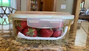 Fresh whole strawberries on a paper towel in a glass container with lid.

