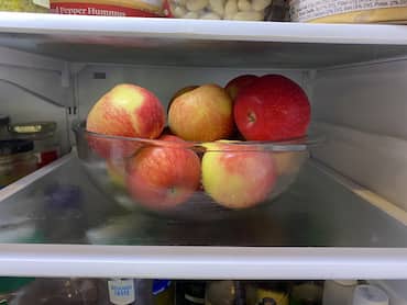 Red apples in a glass bowl in the refrigerator.