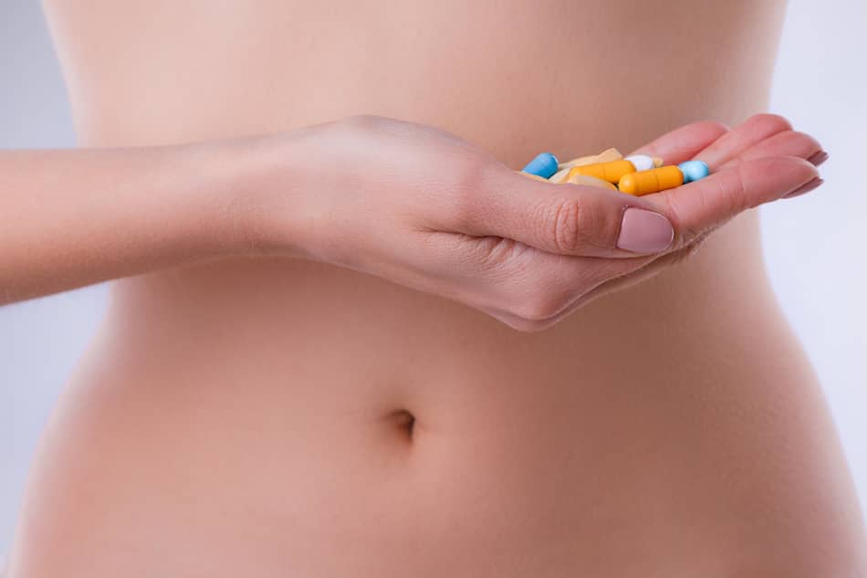 picture of a woman's belly with her hand held in front, holding a number of pills.
