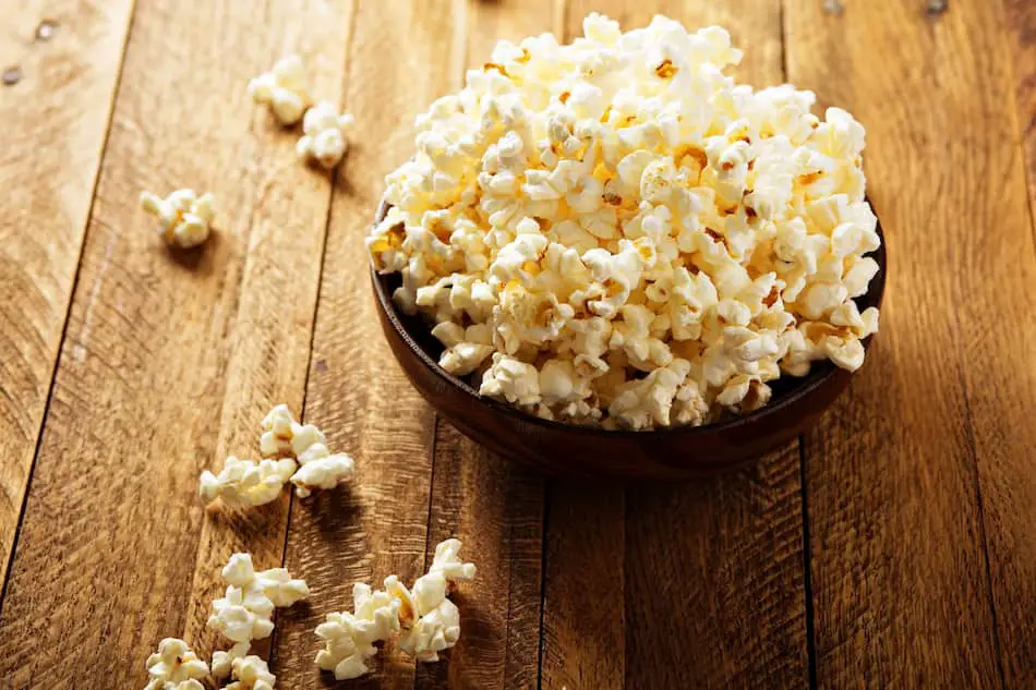 Popped popcorn in a wooden bowl on a wooden table.