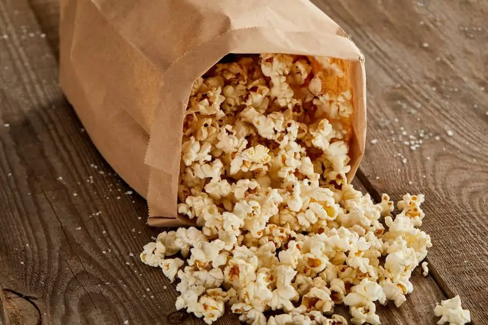 Popped popcorn spilling out of a brown paper bag. 