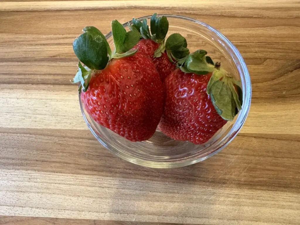 3 fresh strawberries close up in a small glass bowl.